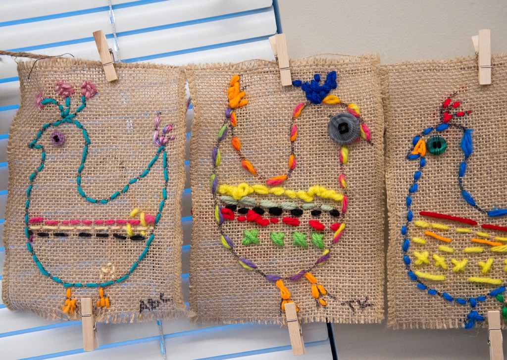 Three examples of 3rd grade students' sewing samplers depicting colorful, whimsical chickens