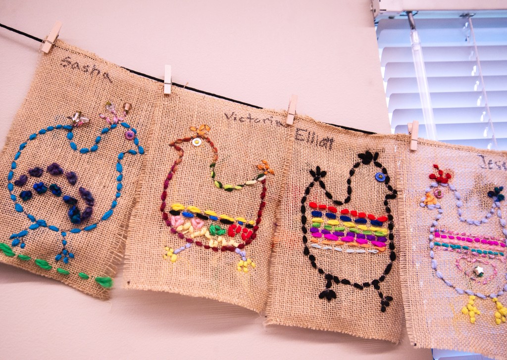 Four examples of 3rd grade students' sewing samplers depicting colorful, whimsical chickens