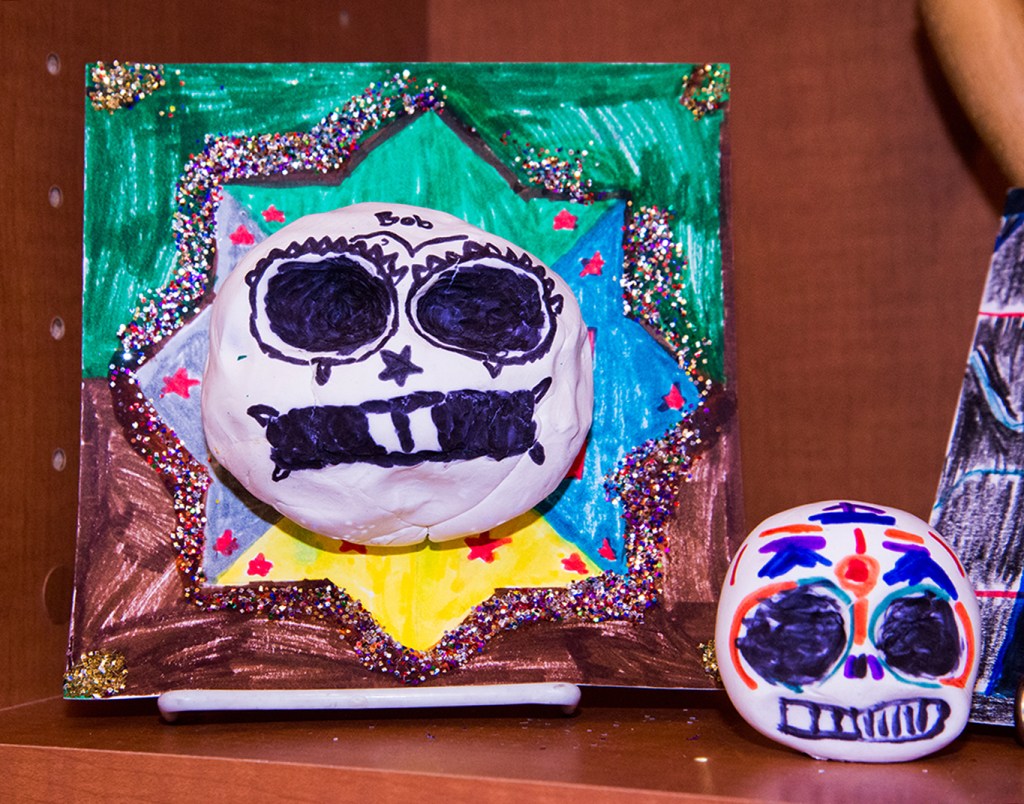 An example of a 4th grade student's clay skull, designed to imitate a Día de los Muertos (Day of the Dead) sugar skull, with a colorful and glittery patterned background