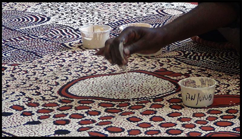 A photograph of an Aborigine applying the dots to a painting.