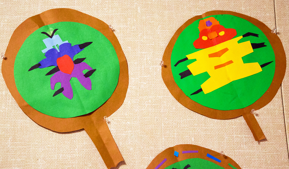 1st grade student examples of insects under a magnifying glass made by collaging colored construction paper with an emphasis on symmetry and contrasting colors.