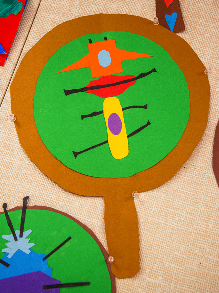 1st grade student example of an insect under a magnifying glass made by collaging colored construction paper with an emphasis on symmetry and contrasting colors.