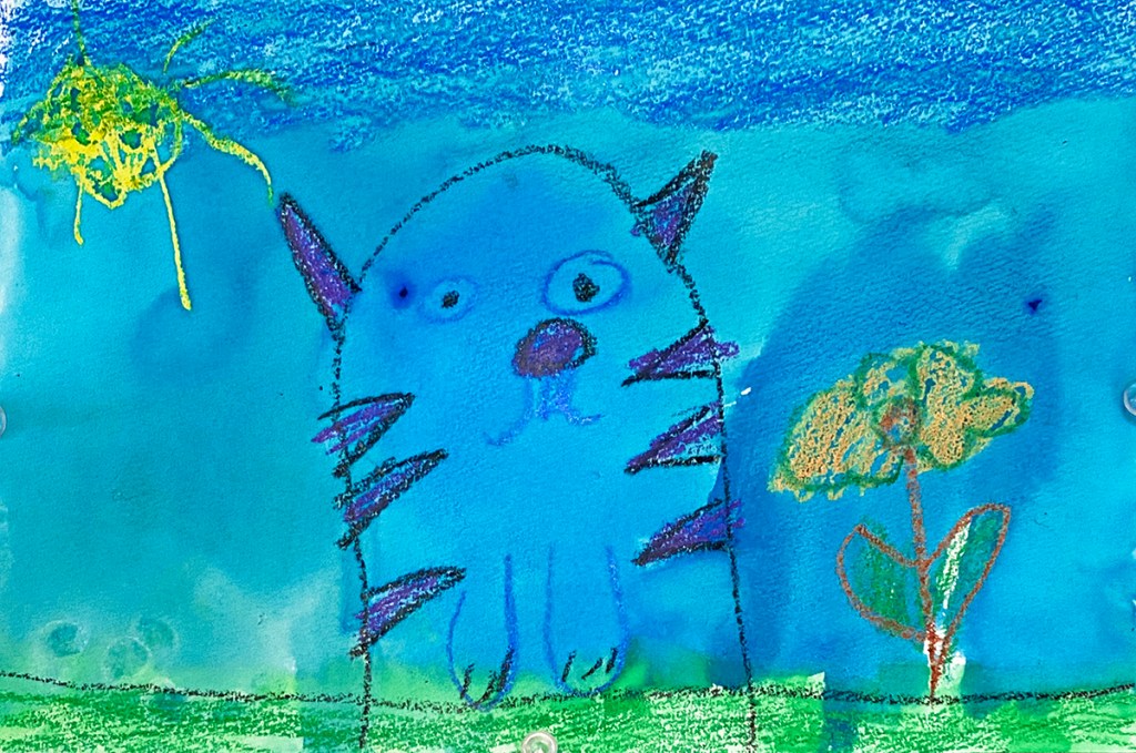 Kindergarten watercolor & crayon resist, finished composition. This shows a blue cat with purple stripes, a flower and a sun on a blue background.