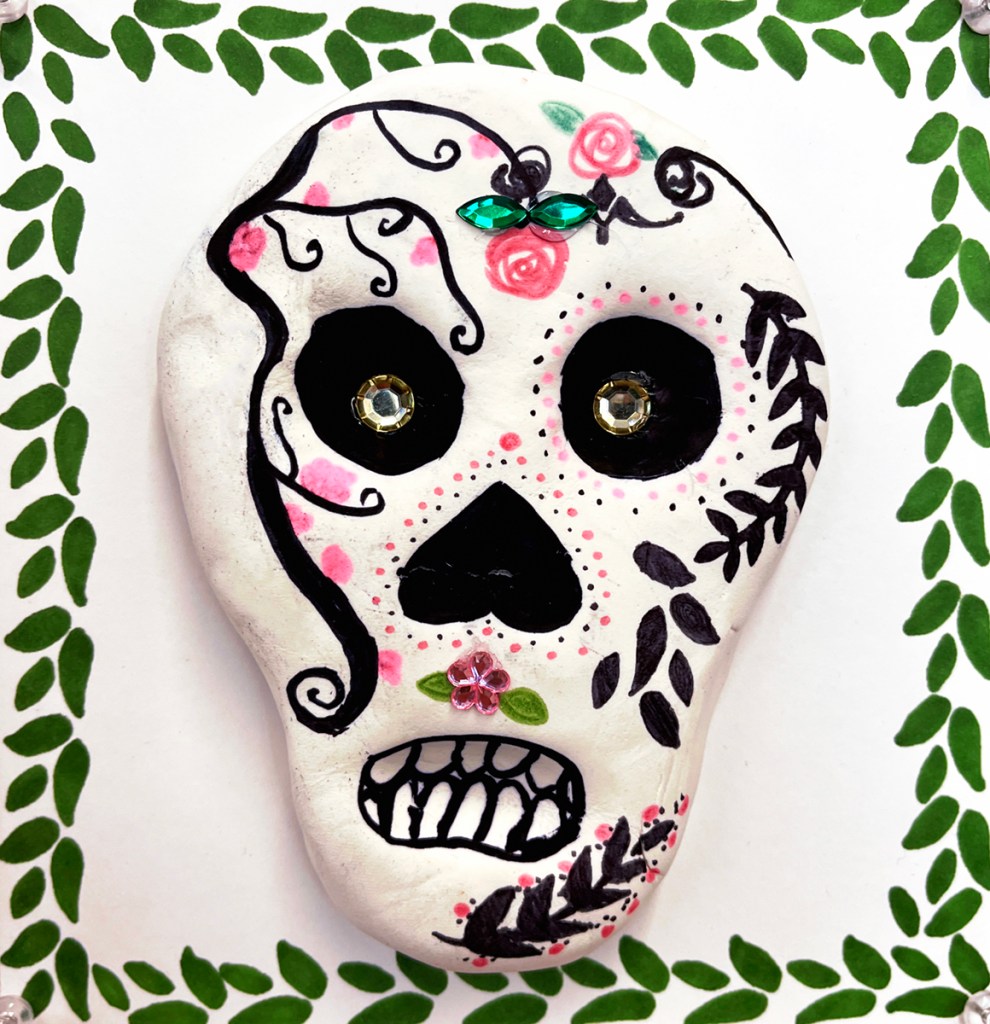 4th grade calaveras- Dia de los Muertos "sugar" skulls made out of model magic clay and decorated in multicolors of markers and sharpies, as well as plastic "gems", and placed on a decorative background in various designs and patterns, also made by the students