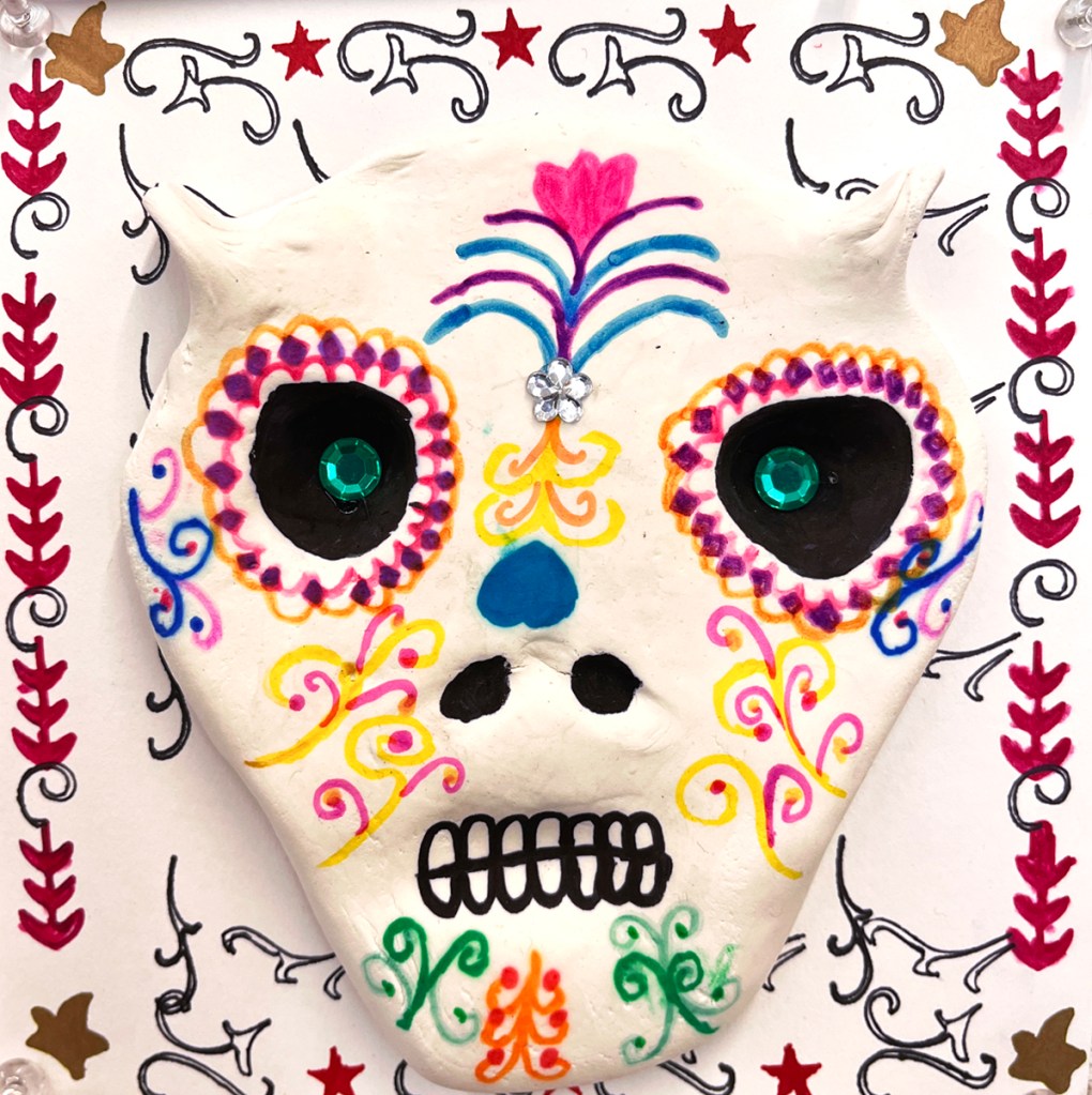 4th grade calaveras- Dia de los Muertos "sugar" skulls made out of model magic clay and decorated in multicolors of markers and sharpies, as well as plastic "gems", and placed on a decorative background in various designs and patterns, also made by the students