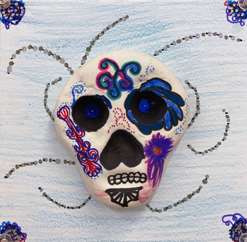 An example of a 4th grade student's clay skull, designed to imitate a Día de los Muertos (Day of the Dead) sugar skull, with a colorful, festive patterned background