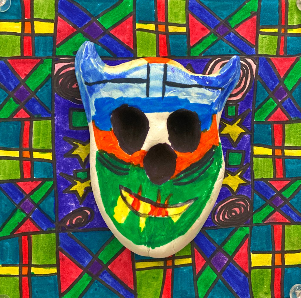 An example of a 4th grade student's clay skull, designed to imitate a Día de los Muertos (Day of the Dead) sugar skull, with a colorful, festive patterned background