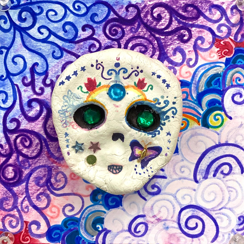 An example of a 4th grade student's clay skull, designed to imitate a Día de los Muertos (Day of the Dead) sugar skull, with a colorful, festive patterned background