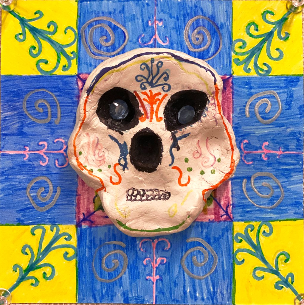 An example of a 4th grade student's clay skull, designed to imitate a Día de los Muertos (Day of the Dead) sugar skull, with a colorful, festive patterned background