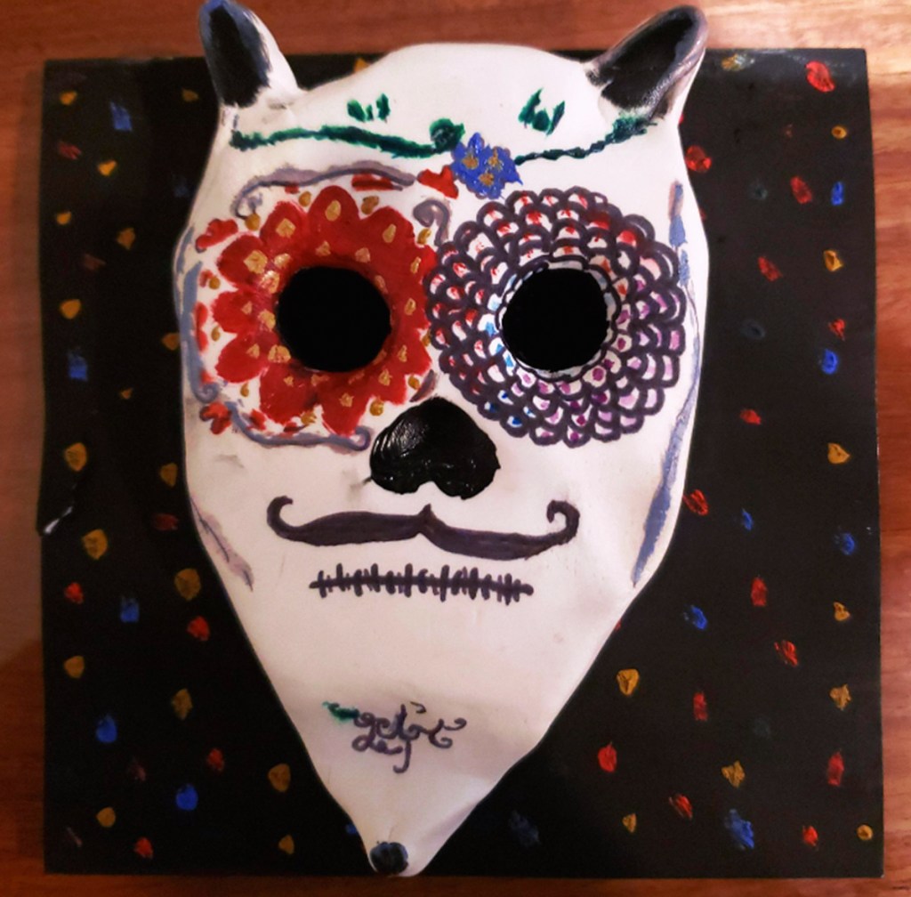 An example of a 4th grade student's clay skull, designed to imitate a Día de los Muertos (Day of the Dead) sugar skull, with a colorful, festive patterned background