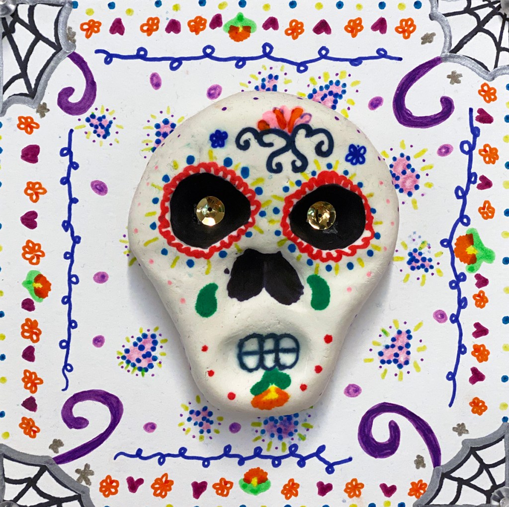 An example of a 4th grade student's clay skull, designed to imitate a Día de los Muertos (Day of the Dead) sugar skull, with a colorful, festive patterned background