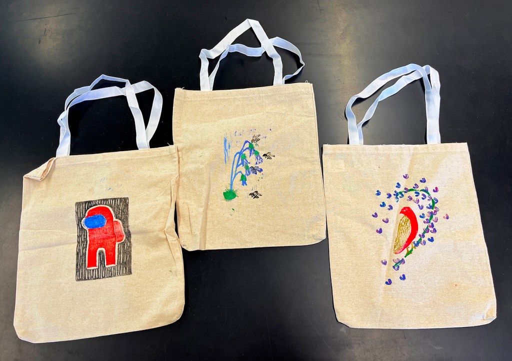Three 8th grade student's canvas tote bags that display their linoleum block prints on the bag.