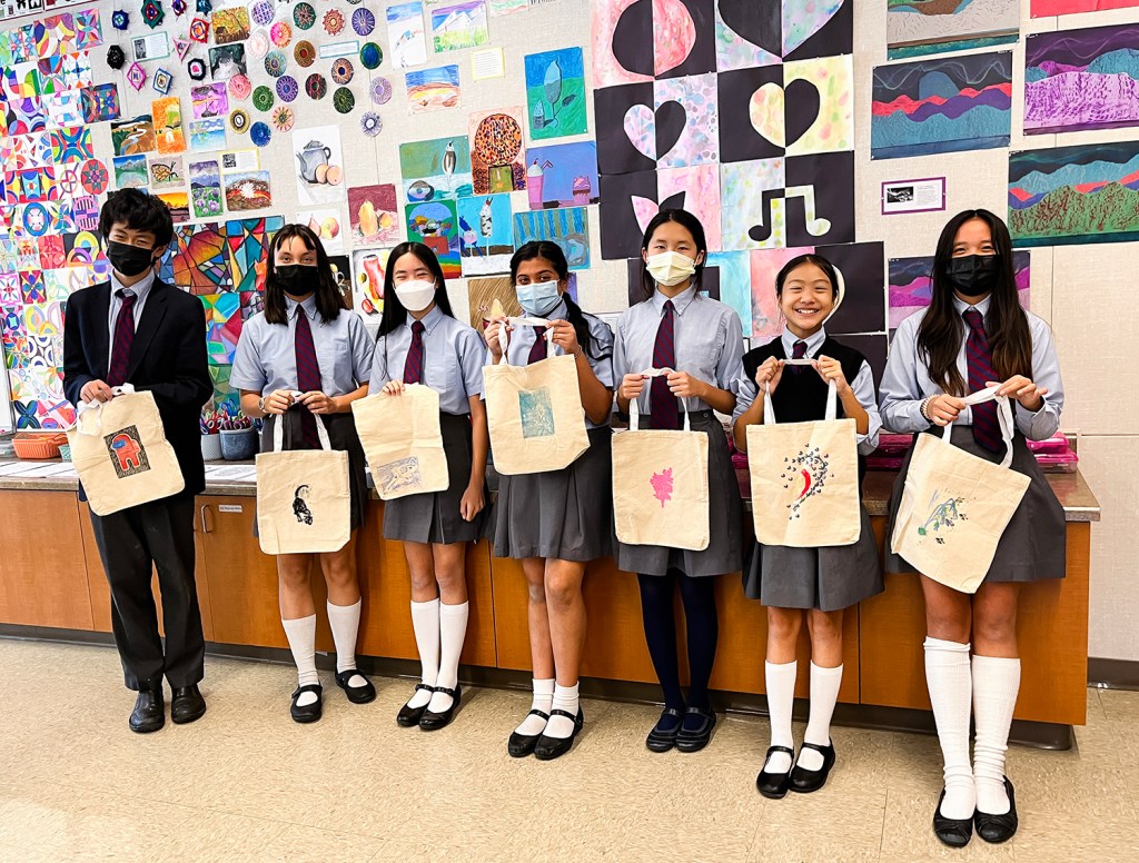 Seven 8th grade students showing off their printed designs on canvas bags