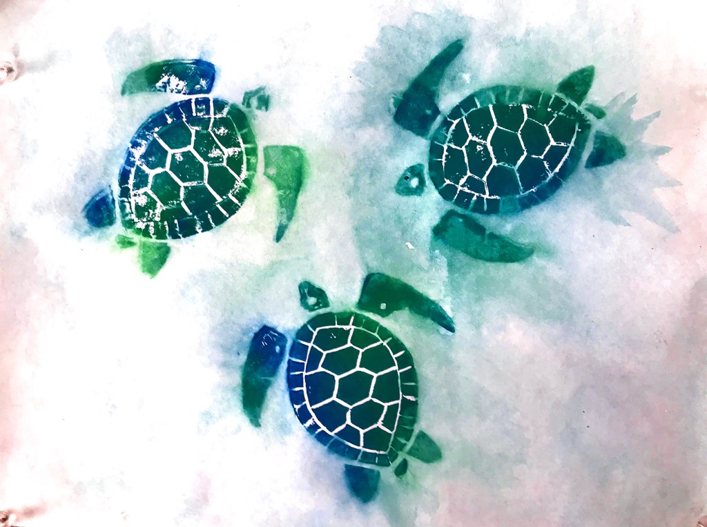 An 8th grade student's linoleum block print. This print displays three blue and green turtles on a watercolor blue-green background.