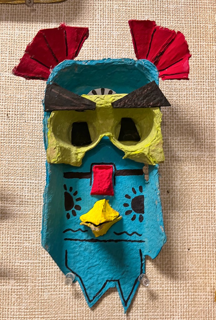 A 6th grade student's masks made of egg cartons, inspired by masks of the pacific Northwest tribes. This one has elaborate designs and decoration, and painted in turquoise, red and green.