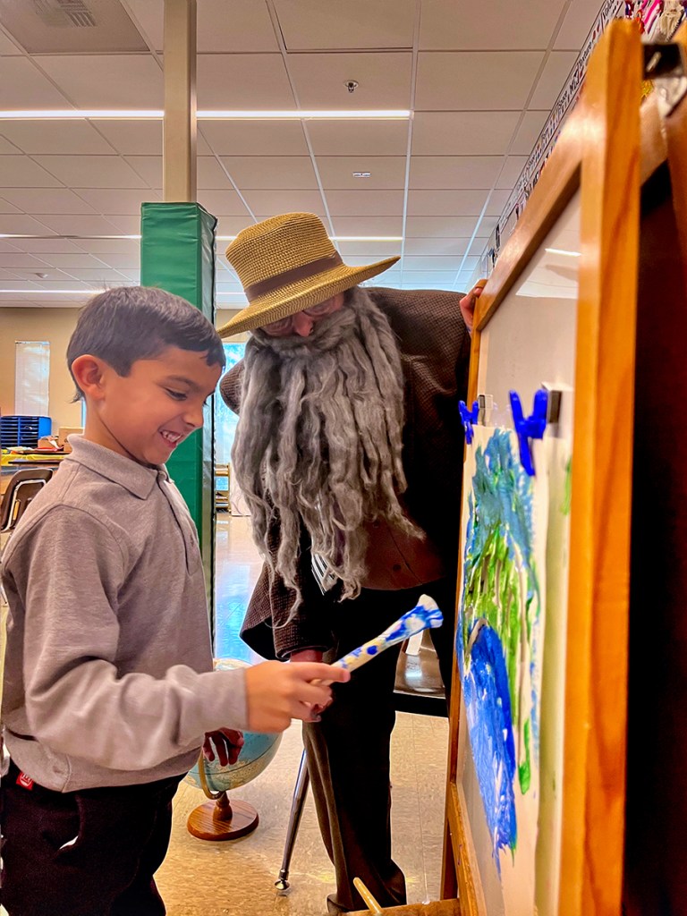 "Monet" (art teacher Willow M), guides a student to paint a version of his 'Bridge over a pond of water lilies' painting