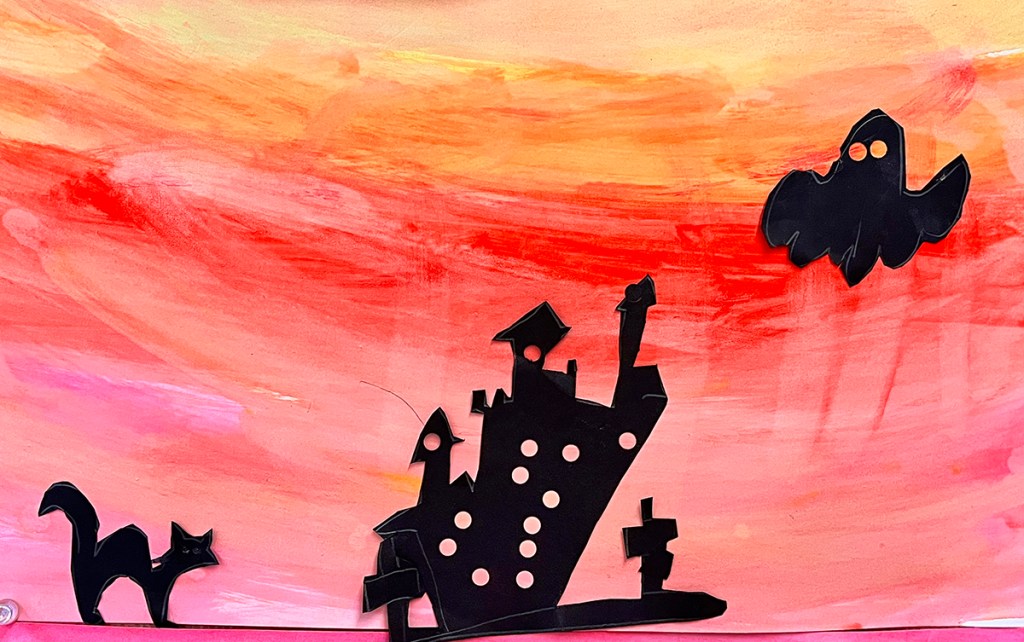 1st grade spooky Halloween scene. Black silhouettes on a painted sunset sky (red, orange, yellow). The silhouettes are of a ghost, a cat, and a haunted house