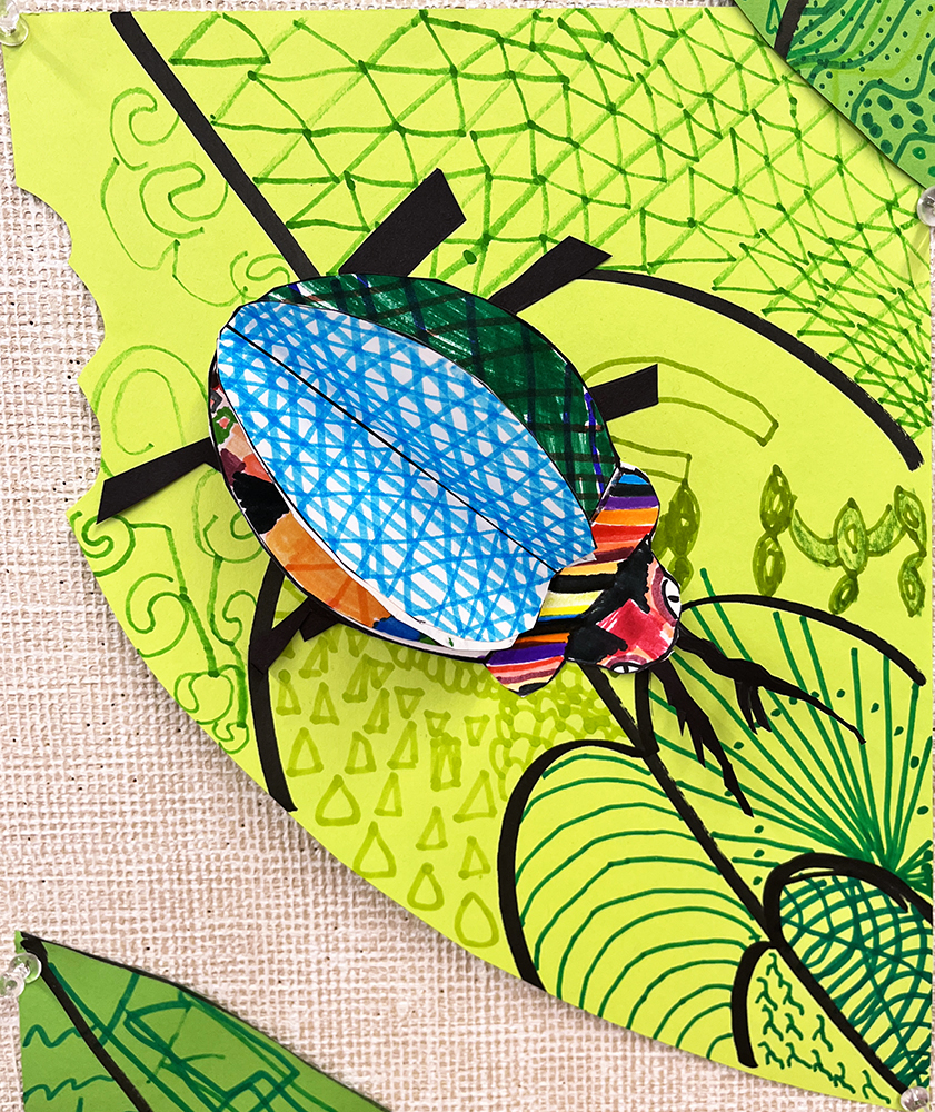 Three-dimensional bug, with vivid colors and diverse patterns on the wings, crawling across a green leaf that itself is covered in varied patterns, created by first grade students