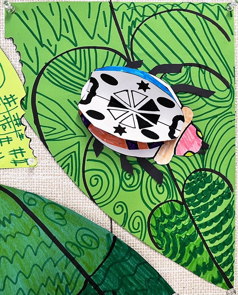 Three-dimensional bug, with vivid colors and diverse patterns on the wings, crawling across a green leaf that itself is covered in varied patterns, created by first grade students